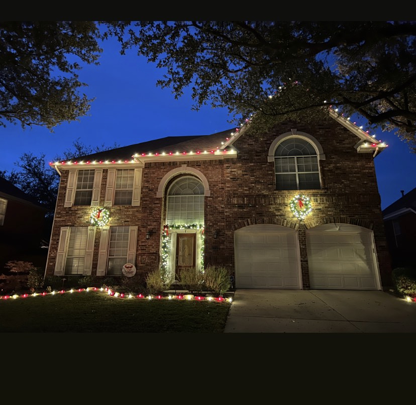 A Lonestar Lux Lighting install — warm-white roofline, lit wreaths, and pathway lighting on a Texas brick home